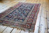 Distressed antique Northwest Persian rug showing dark blue Herati field, red border, and fringe.