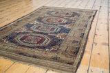 Textured geometric medallions and tribal motifs of the antique Belouch rug in navy, chestnut, and tobacco.