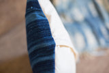 Finely handwoven dark blue striped indigo textile next to a cream cotton canvas pillow backing.