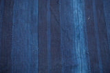 Hand woven African indigo textile detail, showing variegated blue stripes and visible seams.