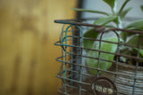 Close-up of vintage wire basket with rusted brown and teal-blue wires and circular tag.