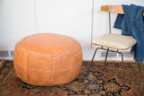 Camel brown leather pouf displaying embossed fleur de lis and flower fan patterns.