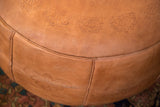 Distressed camel brown leather Moroccan pouf featuring flower fan and fleur de lis stenciling.