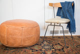 Camel brown Moroccan leather pouf, featuring distressed texture and stenciled fleur de lis patterns.