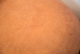 Close-up of camel brown leather pouf showcasing distressed texture and flower fan stenciling.