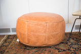 Camel brown leather pouf's lower side, showing fleur de lis stenciling and distressed texture.