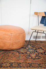 Camel brown leather pouf with stamped fleur de lis, atop an antique Persian rug.