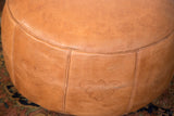Distressed camel brown leather pouf with fleur de lis and fan stenciling.