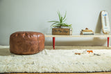 Distressed natural brown leather Moroccan pouf with fleur de lis and flower stenciling.
