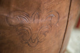 Distressed natural brown leather pouf with decorative stenciled flourishes.