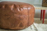 Natural brown Moroccan leather pouf showing stenciled fleur de lis and subtle distressing.
