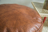 Natural brown distressed leather Moroccan pouf with antique revival floral fan stenciling.