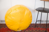 Fly yellow Moroccan leather pouf with prominent side stitching and lacing.