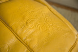 Close-up of mustard yellow distressed leather Antique Revival Moroccan pouf with fleur de lis.