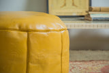 Mustard yellow leather pouf with embossed fleur de lis and subtle distressing.