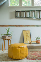 Mustard yellow Moroccan leather pouf with stenciled patterns and distressed leather texture.