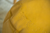 Close-up of textured mustard yellow Moroccan leather pouf with flower fan stenciling.