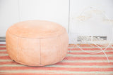 Nude distressed leather pouf ottoman with floral and fleur de lis stenciling.