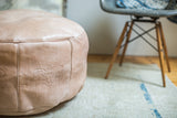 Lightly distressed nude leather pouf showing embossed fleur de lis and fan stencils.