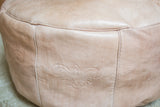 Distressed nude leather pouf with debossed fleur de lis and stitched panel.