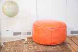 Tangerine orange Moroccan leather pouf ottoman with fleur de lis stenciling.