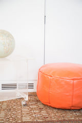 Tangerine orange leather pouf ottoman side view, showcasing fleur de lis and flower fan stenciling.
