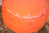 Close-up of tangerine orange Moroccan pouf's leather, embossed flower fan, and stitched seam.