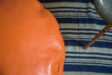 Tangerine orange leather pouf, featuring subtle flower fan stenciling and texture.