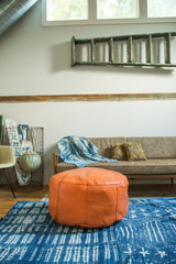Tangerine orange Moroccan leather pouf ottoman with distinctive fleur de lis stenciling.