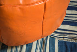 Tangerine orange leather pouf detail shows subtle debossed floral pattern.