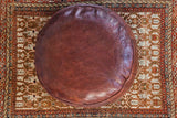 Round Antique Revival Dark Whiskey Moroccan pouf with distressed leather and stenciled motifs.