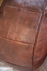 Dark whiskey leather Moroccan pouf detail with stenciled fleur de lis and texture.