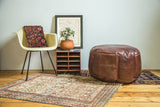 Whiskey brown leather pouf with subtle fleur de lis stenciling and distressed texture.