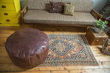 Whiskey brown Moroccan leather pouf with stenciled designs and distressed texture.