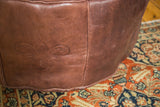 Embossed fleur de lis and flower fan on distressed whiskey brown leather pouf.