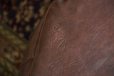 Distressed whiskey brown leather pouf with embossed flower fan detail.