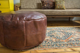 Detail of whiskey brown Moroccan leather pouf with fleur de lis stencil design.
