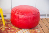 Distressed cherry red leather pouf with fleur-de-lis and flower fan stenciling, bottom lacing.