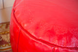 Cherry red Moroccan leather pouf close-up, embossed flower fan stenciling, distressed texture.