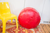 Detail view of the cherry red leather pouf, highlighting bottom lacing and distressed texture.