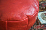 Distressed cranberry red leather Moroccan pouf, impressed floral fan design.