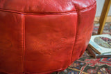 Close-up of cranberry red Moroccan pouf, highlighting distressed leather and fleur de lis stenciling.