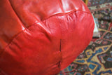 Cranberry red Moroccan leather pouf showcasing hand-crafted lacing and distressed texture.