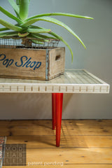 Corner detail of the Mod Sled Table's wood slat construction and vibrant red tapered legs.