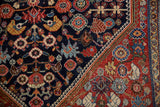 Antique Qashqai rug corner: intricate navy field patterns meet a vibrant ruby red border.