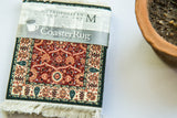 Packaged Shah Jahan CoasterRug showing intricate red floral design and cream border.