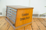 Antique Eureka Spool Silk cabinet, showing glass drawers and side text on aged oak.