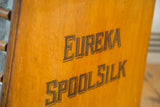 Clear EUREKA SPOOL SILK lettering on the aged oak Victorian spool cabinet.