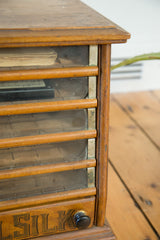 Victorian Eureka cabinet's lower drawer with 'SILK' text, black knob, aged glass.