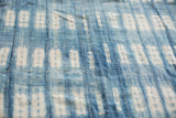 Close-up of hand-woven indigo textile with blue and white resist-dyed patterns and visible stitching.